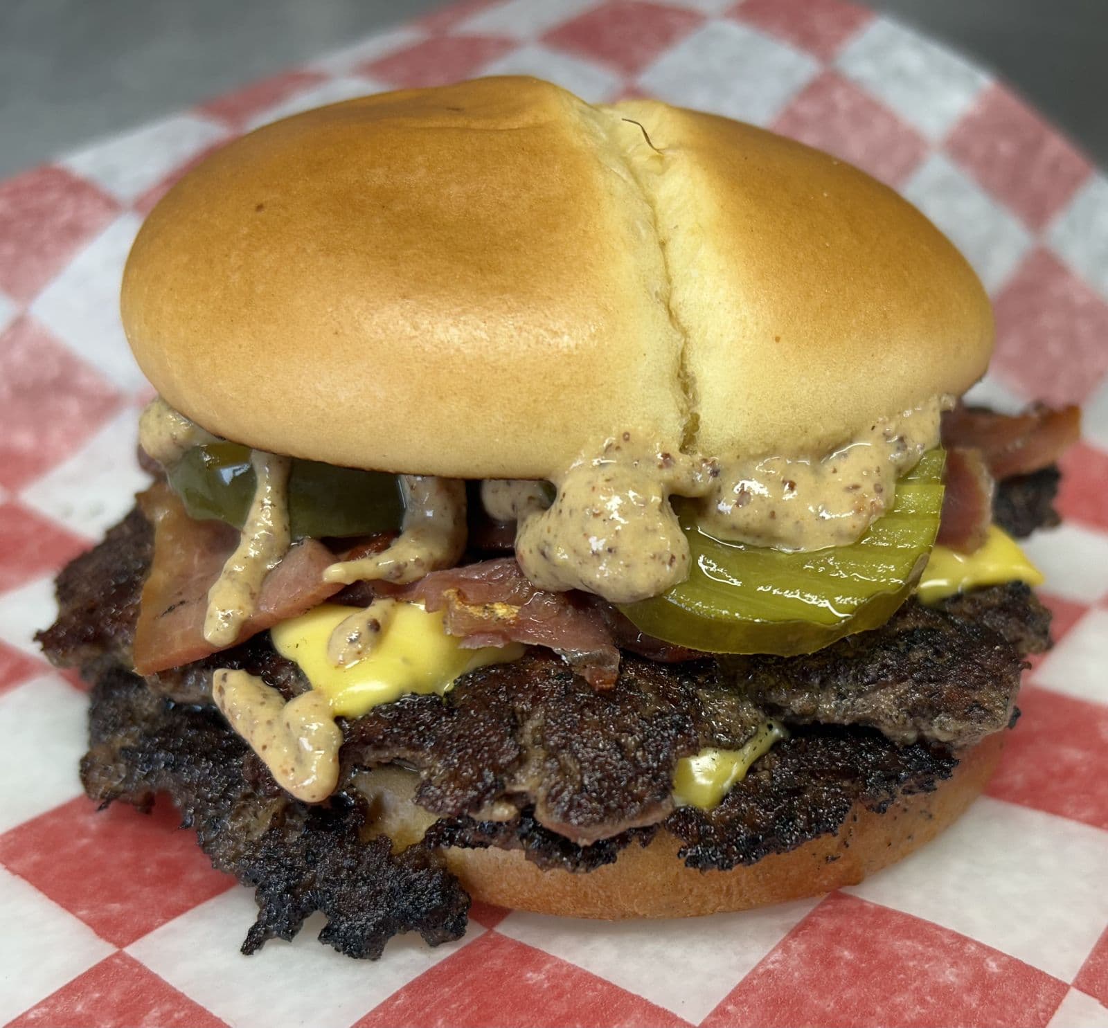 A bacon smashburger with mustard-seed sauce and pickles from The Wurst, on red-and-white checked paper